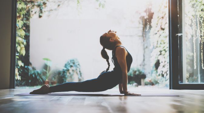 Portrait of gorgeous young woman practicing yoga indoor. Beautiful girl practice cobra asana in class.Calmness and relax, female happiness.Horizontal, blurred background.Visual effects